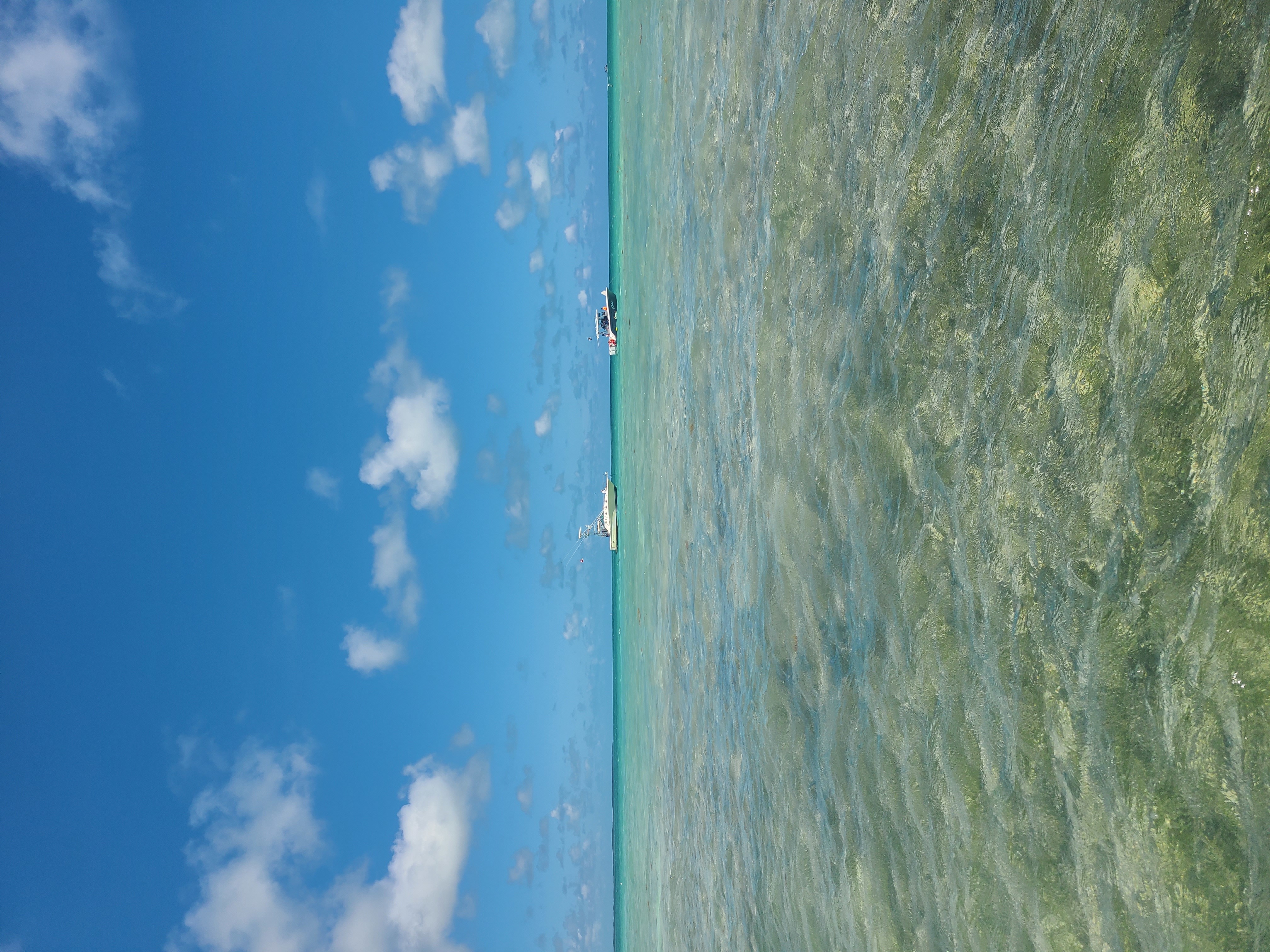 The picture shows the Florida Keys ocean on a sunny day, light teal colored water with bright blue skies and white clouds casting shade over the sea